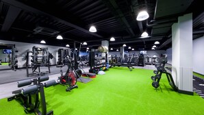 Une salle de sport dotée d’un sol vert, de divers appareils d’exercice et d’un éclairage au plafond.