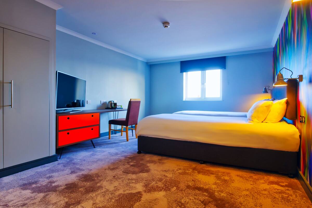 A bedroom with a bed, a desk, a chair, and a television.