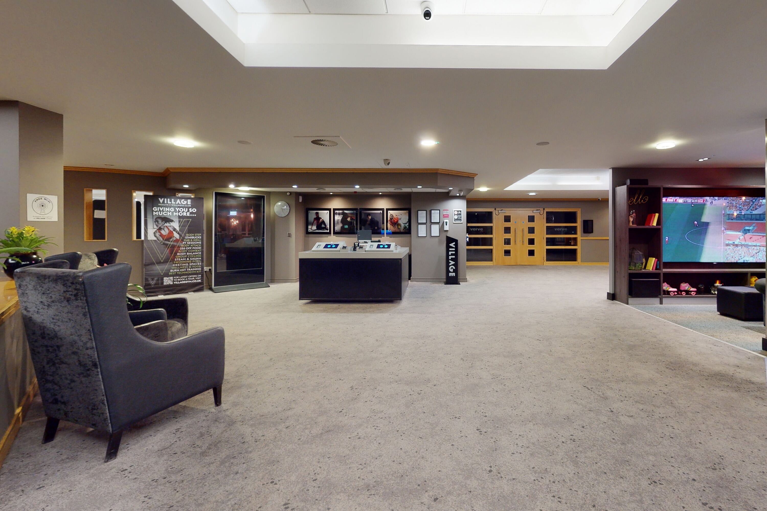 A spacious lobby with a reception desk, seating area, and a large screen displaying a sports event.