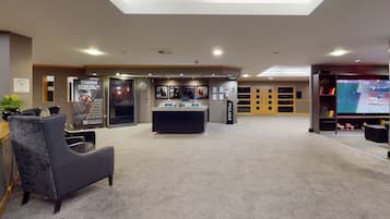 A spacious lobby with a reception desk, seating area, and a large screen displaying a sports event.