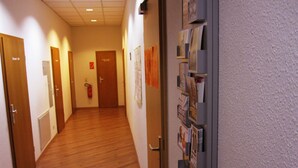 Un pasillo con suelo de madera, puertas a ambos lados y un tablón de anuncios a la derecha.