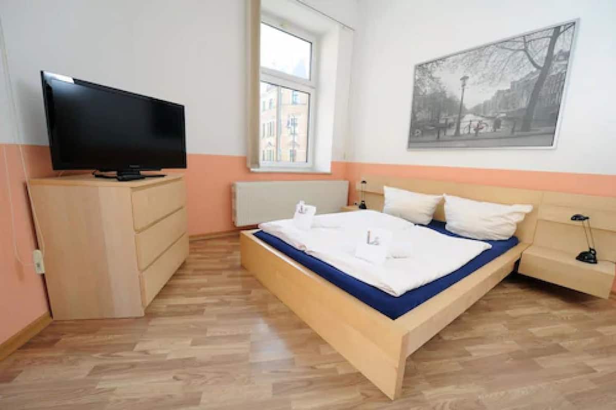 A bedroom with a bed, a TV on a dresser, a window, and a wall-mounted picture.