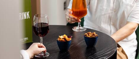 En person holder et glas øl ved et bord med to skåle med snacks.