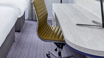 A hotel room with a bed, a desk, a chair, and a carpeted floor.