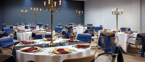 A conference room with round tables, blue chairs, and gold candelabras.