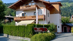 A two-story hotel with a balcony, a sign indicating it is the "Hotel Reithwirt," and a view of the surrounding green hills. - Hotel Reitlwirt (Brixen im Thale)