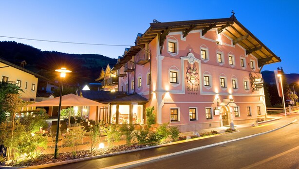 A pink building with multiple windows and a balcony, surrounded by outdoor seating and plants. - Hotel Reitlwirt (Brixen im Thale)
