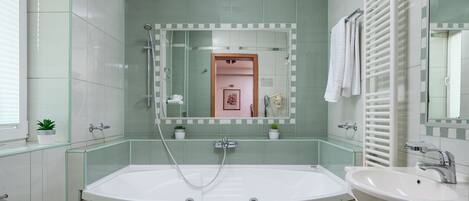 A modern bathroom with a large bathtub, a sink, and a mirror. There are two small potted plants on the countertop.