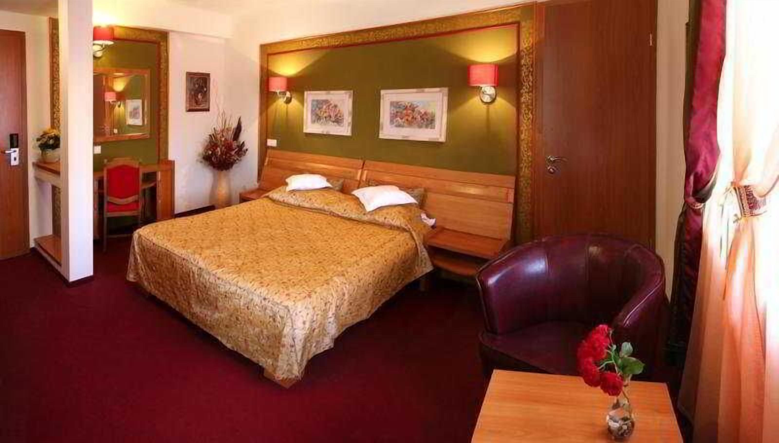 Una habitación de hotel con una cama grande, un cabecero de madera, un escritorio con una silla y un jarrón con flores.