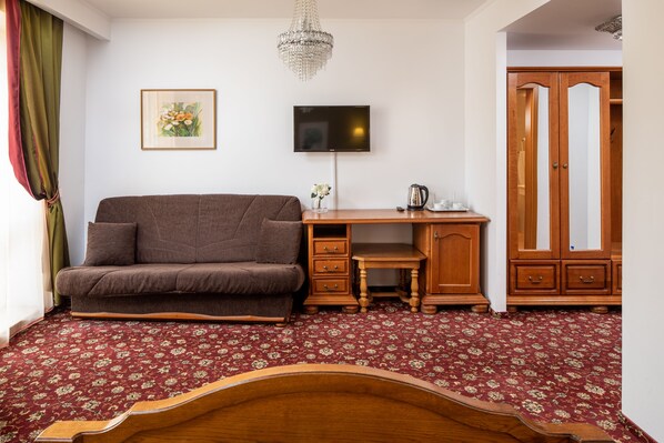 Una habitación con sofá, escritorio, televisor, armario y alfombra estampada.