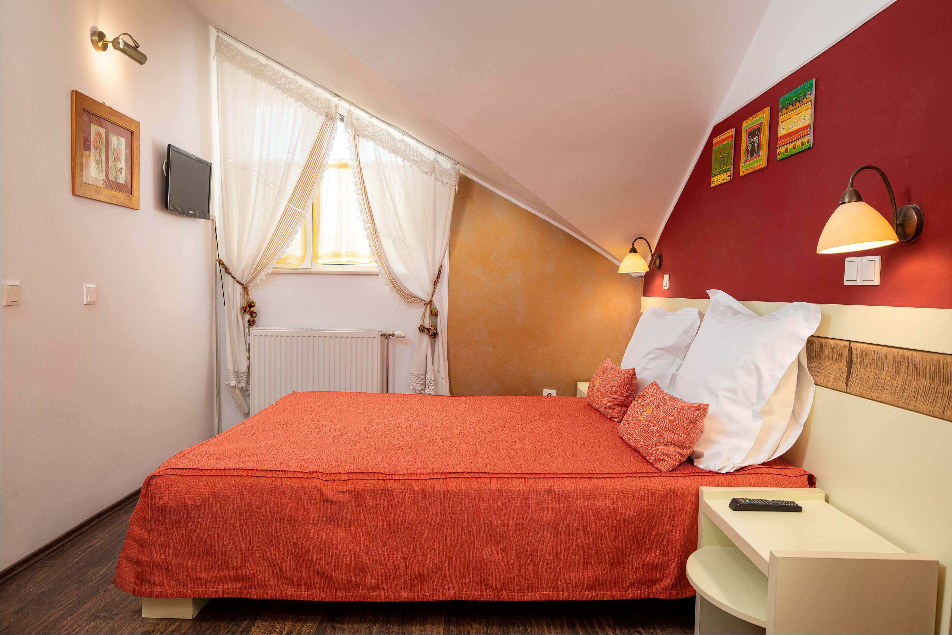 A bedroom with a bed, a nightstand, a lamp, a window with curtains, and wall decorations.