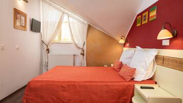 A bedroom with a bed, a nightstand, a lamp, a window with curtains, and wall decorations.