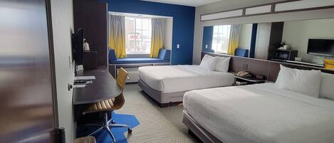 Una habitación de hotel con cama, escritorio, silla, televisor y ventana con cortinas.