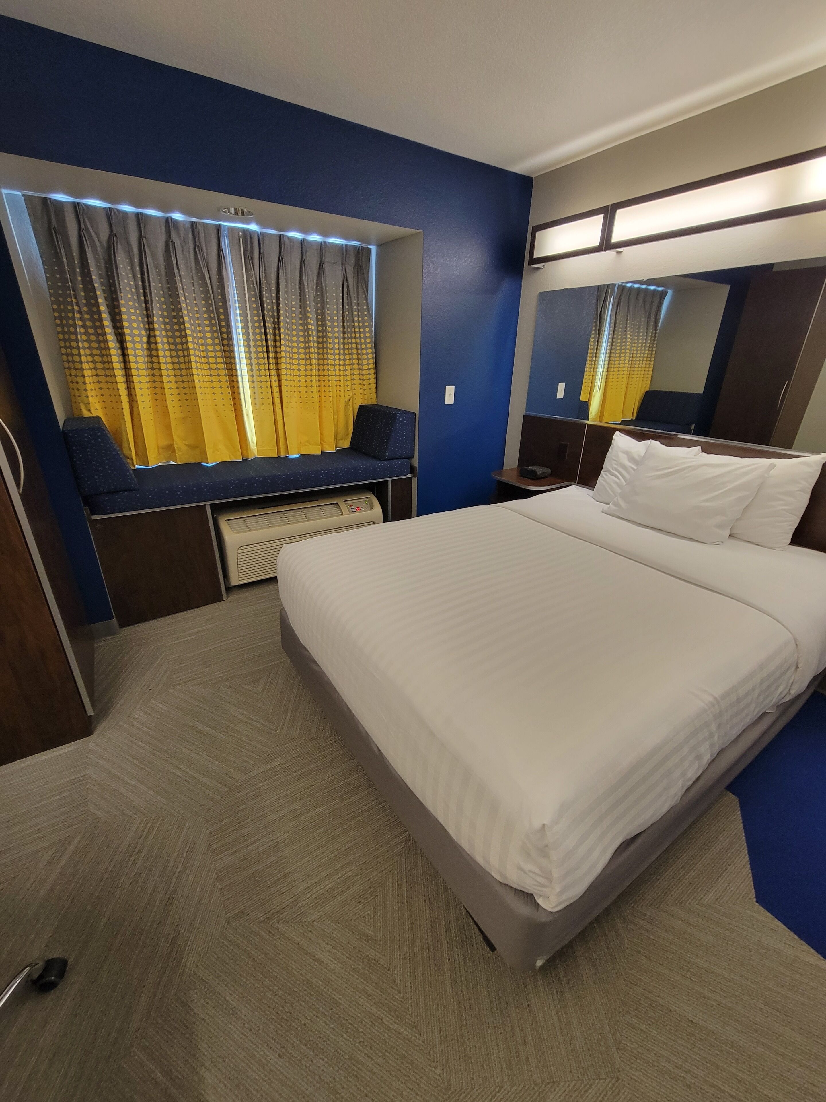 A hotel room with a bed, a seating area with a desk, a heater, and a large mirror.