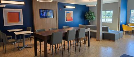 Un moderno vestíbulo de hotel con una gran mesa de conferencias, varias sillas, un televisor y una planta en maceta.