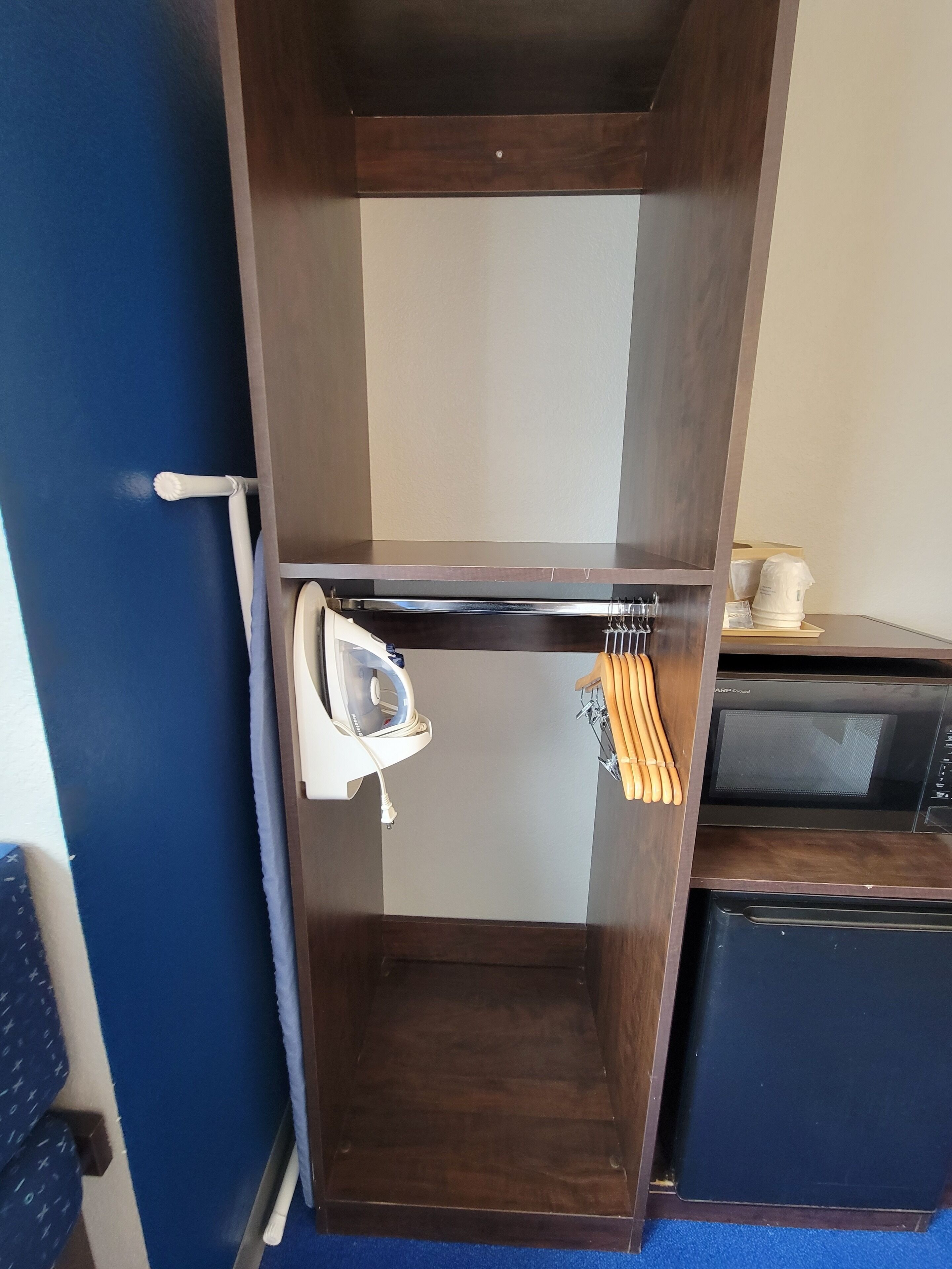 Una kitchenette compacta con microondas, plancha y un tendedero.