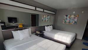 Habitació d'hotel amb dos llits, escriptori, cadira, televisió i obra d'art a les parets.
