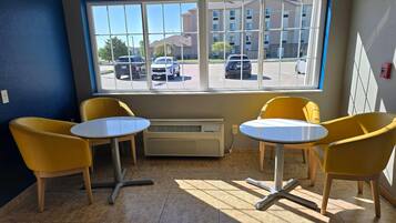 A room with two yellow chairs and a small table, a window with a view of a parking lot and buildings, and an air conditioning unit on the wall.