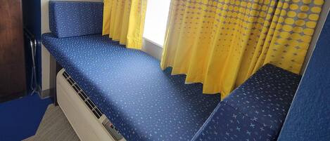 A room with a bed, a window with curtains, and a ceiling light.
