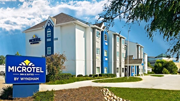 Edifici d'un Microtel Inn & Suites amb façana blava i blanca, un jardí ben cuidat i un panell informatiu.