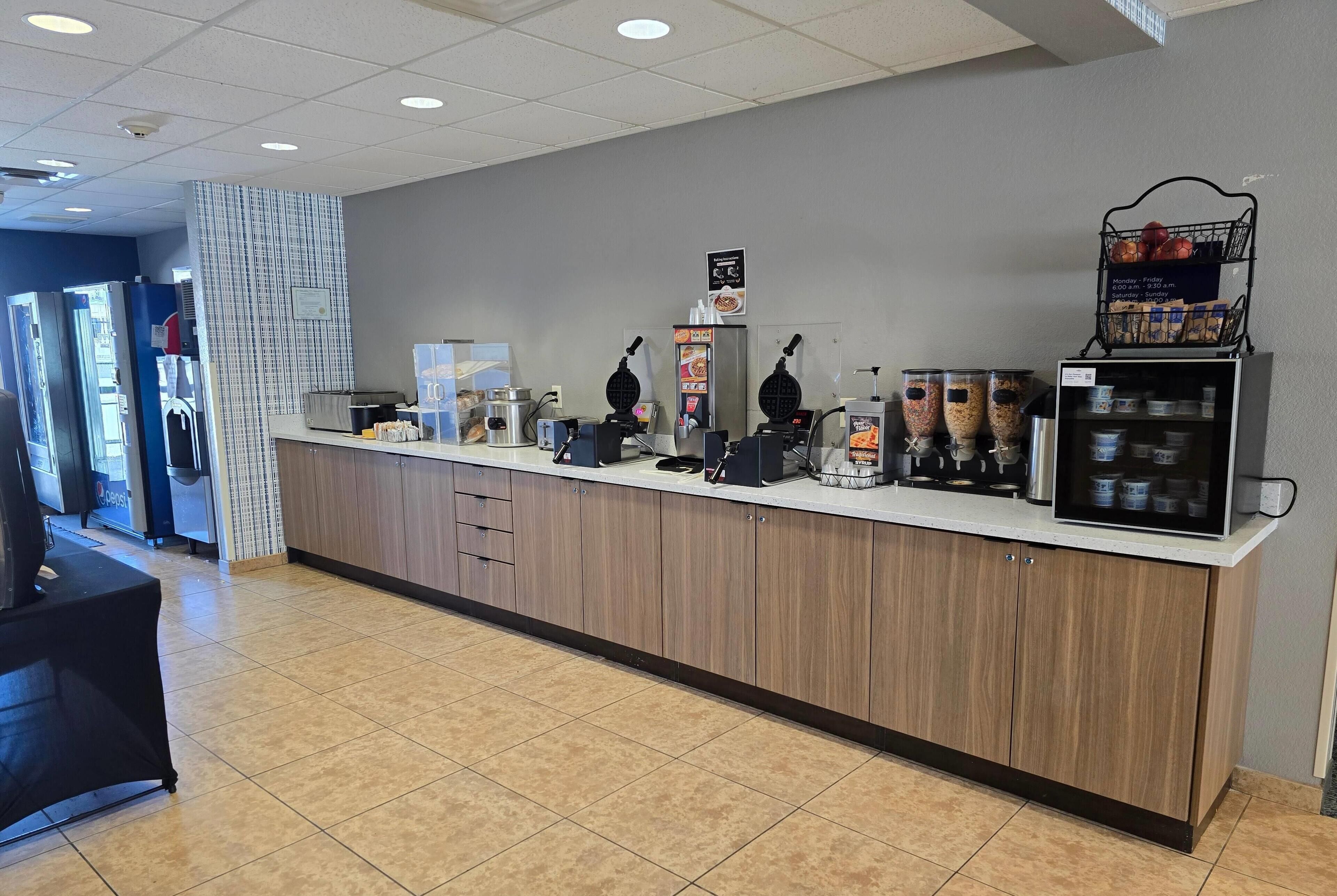 A clean, well-lit food service area with a counter, waffle maker, and beverage dispensers.