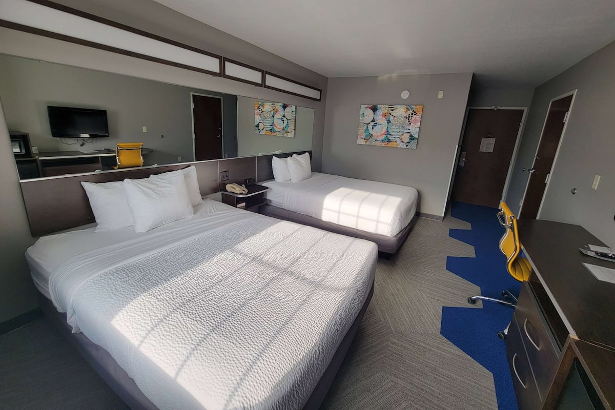 A hotel room with two beds, a desk with a chair, a TV, and artwork on the walls.