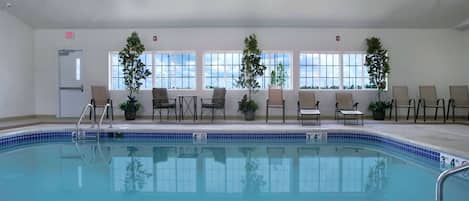 An indoor swimming pool with clear blue water, surrounded by lounge chairs and potted plants.