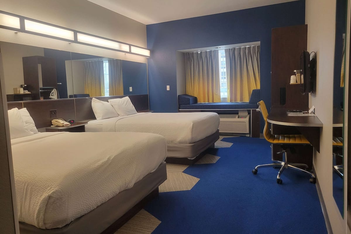 A hotel room with two beds, a desk, a chair, a TV, and a window with curtains.