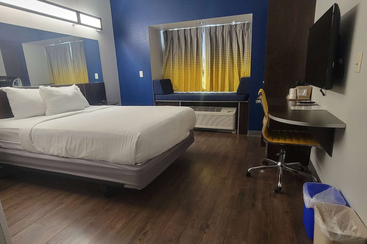 A hotel room with a bed, a desk, a chair, a TV, and a window with curtains.