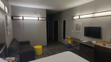 Habitación de hotel con cama, escritorio, silla, televisión y una pequeña mesa con teléfono.