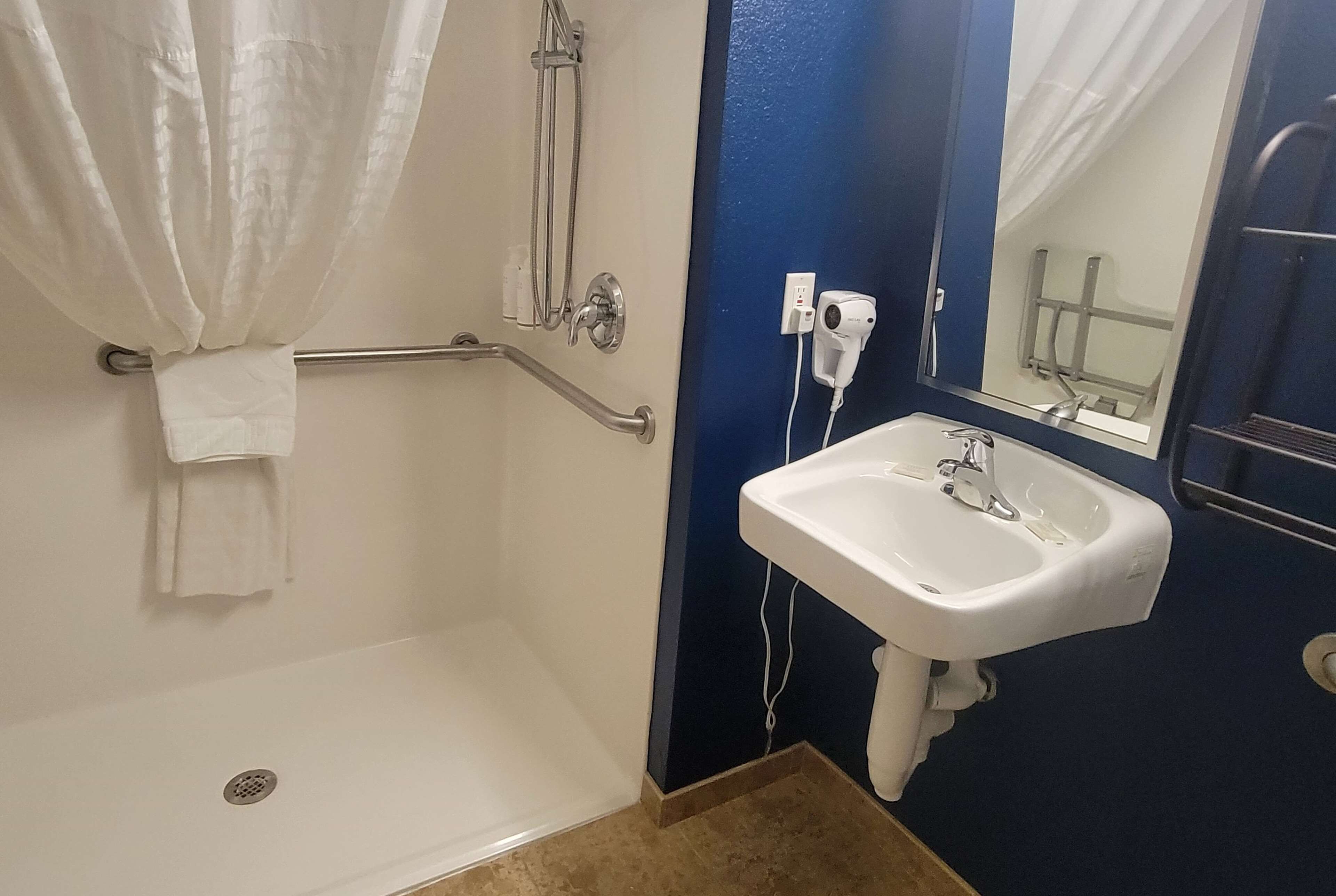 Een badkamer met een douche, een witte wastafel, een handdoekhouder en een spiegel.