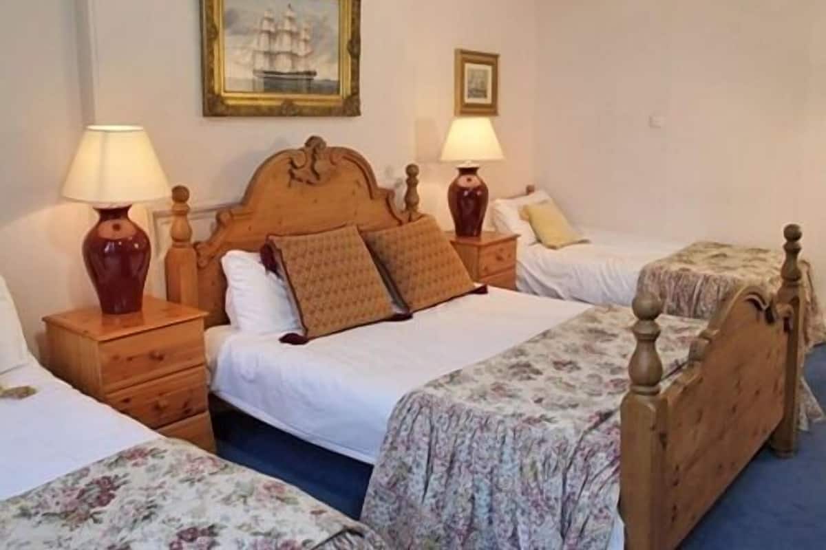A hotel room with two single beds, each with a wooden headboard, a nightstand, and a lamp. There is a framed picture on the wall above the beds.