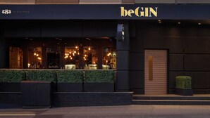 A building with a 'beGIN' sign, featuring a dark facade, a wooden door, and a well-lit interior with visible lights and a bar area. - The Georgian House Hotel (Glasgow)