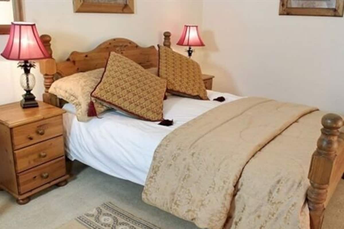 A bedroom with a wooden bed, two bedside tables with lamps, a patterned rug, and a wooden headboard.