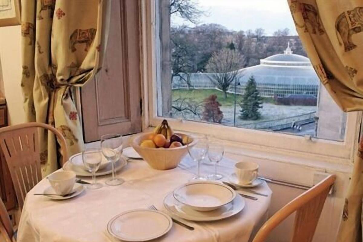 A dining table set for two with a bowl of fruit, plates, and cutlery.