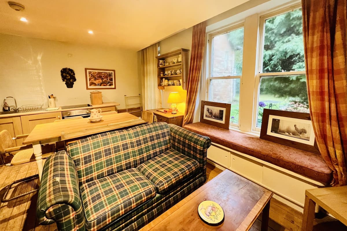 A cozy living room with a plaid sofa, a wooden coffee table, and a window with curtains.