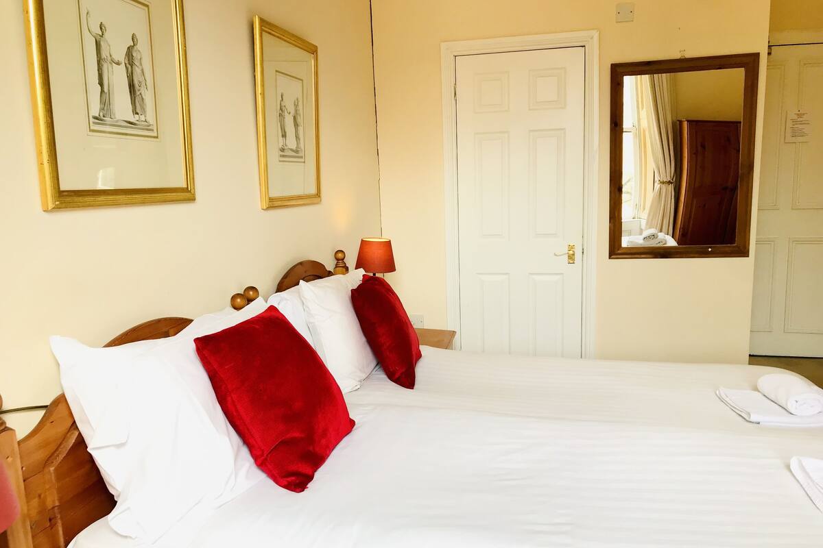 A hotel room with two beds, a wooden headboard, a white door, and two framed pictures on the wall.