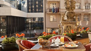 A dining table with breakfast items, a decorative fountain, and potted plants in a hotel setting.
