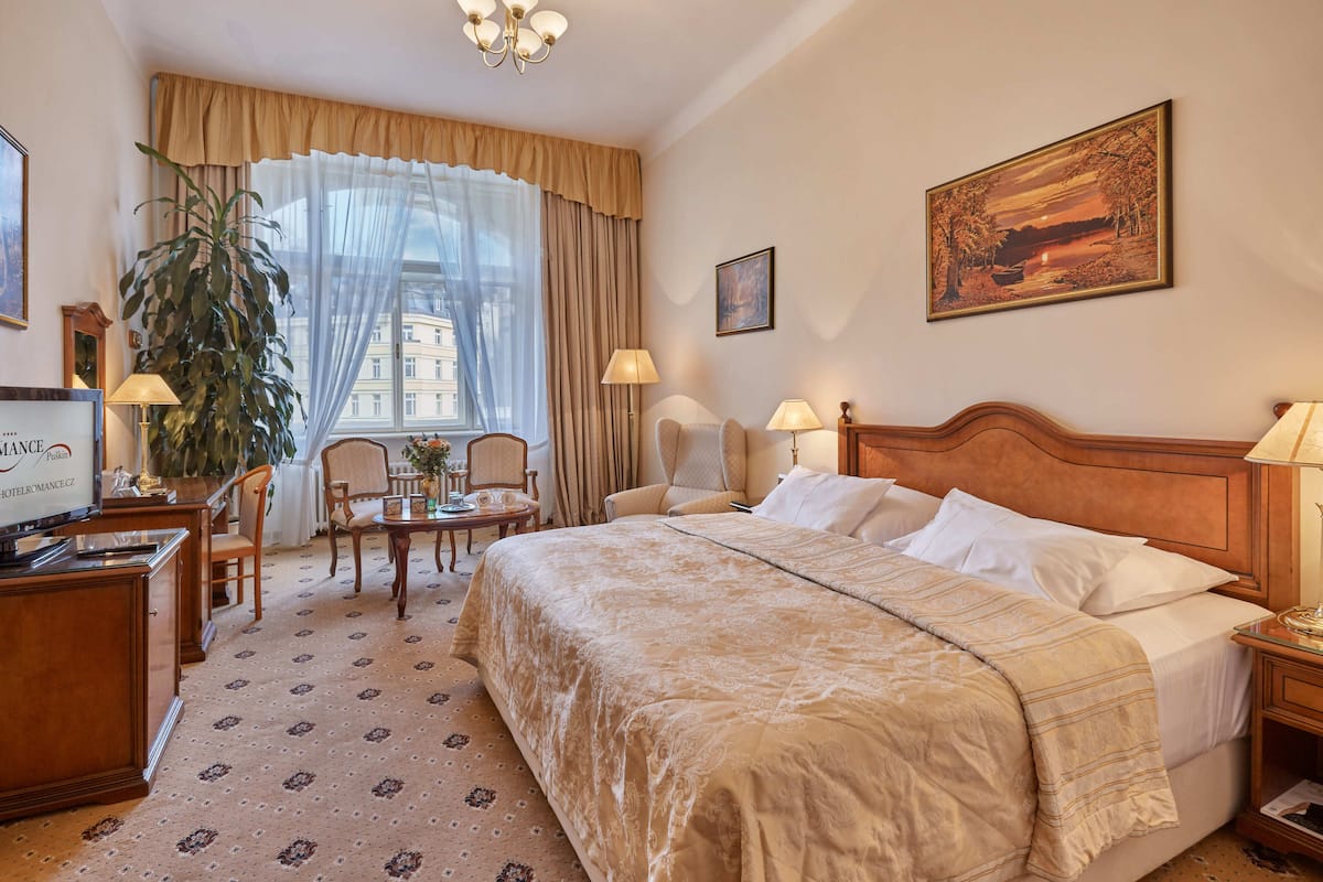 Ein Hotelzimmer mit einem großen Bett, einem Schreibtisch, einem Stuhl, einem Tisch und einem großen Fenster mit Vorhängen.
