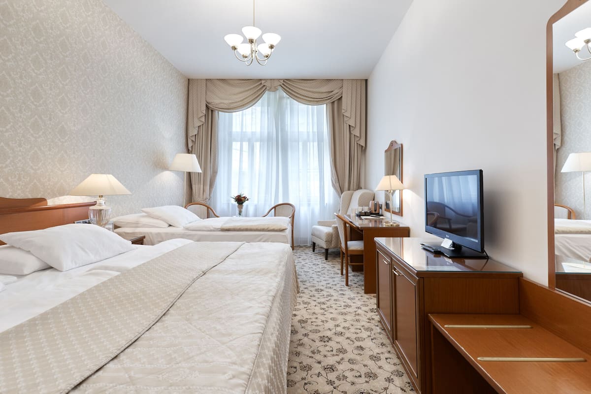 Ein Hotelzimmer mit zwei Betten, einem Schreibtisch mit Fernseher, einem Sessel und einem Spiegel.