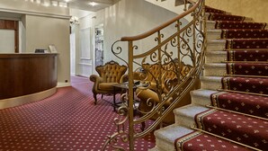 A grand staircase with ornate metal railings, a chandelier, and red carpeted steps.