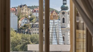A view through a window with curtains, revealing a building with a clock tower and a modern glass structure.