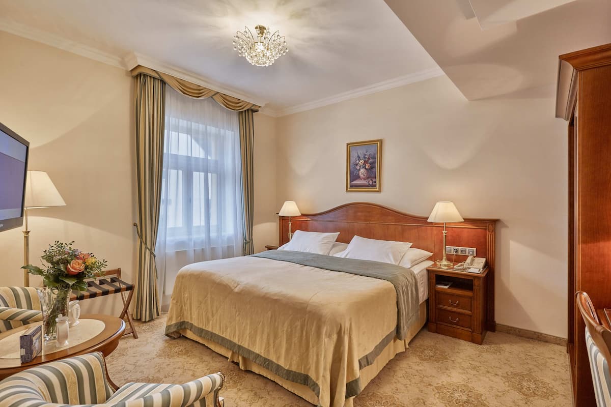 Ein Hotelzimmer mit einem großen Bett, zwei Nachttischen, einem Fernseher, einem Schreibtisch mit Stuhl und einer Kristallleuchter.