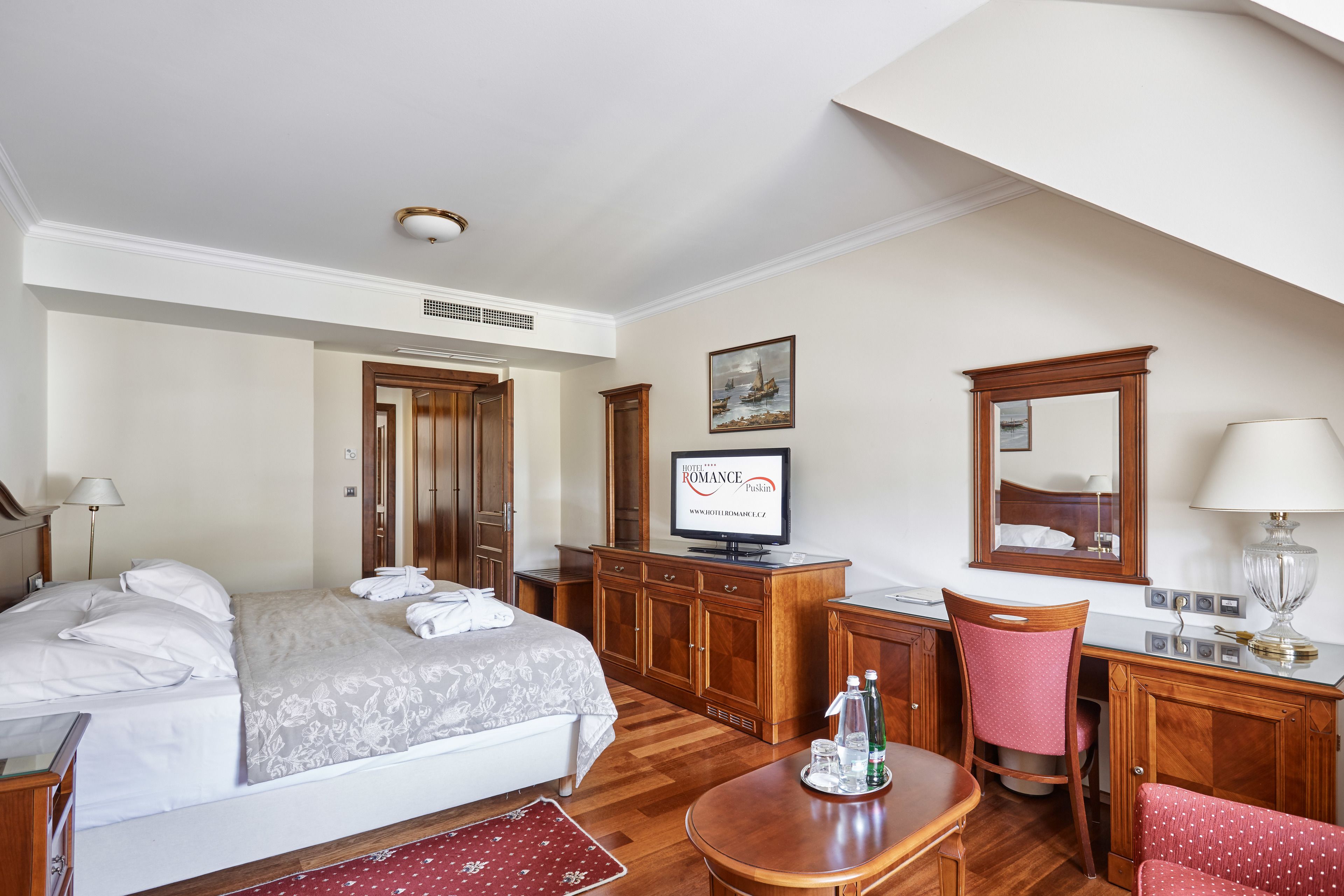 Una habitació d'hotel amb un llit, una taula de treball, una cadira, un televisor i un mirall.