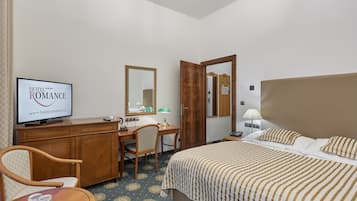 Hotellihuone, jossa on sänky, työpöytä, tuoli, televisio, jossa näkyy elokuva nimeltä ”HOTEL ROMANCE”, ja peili.