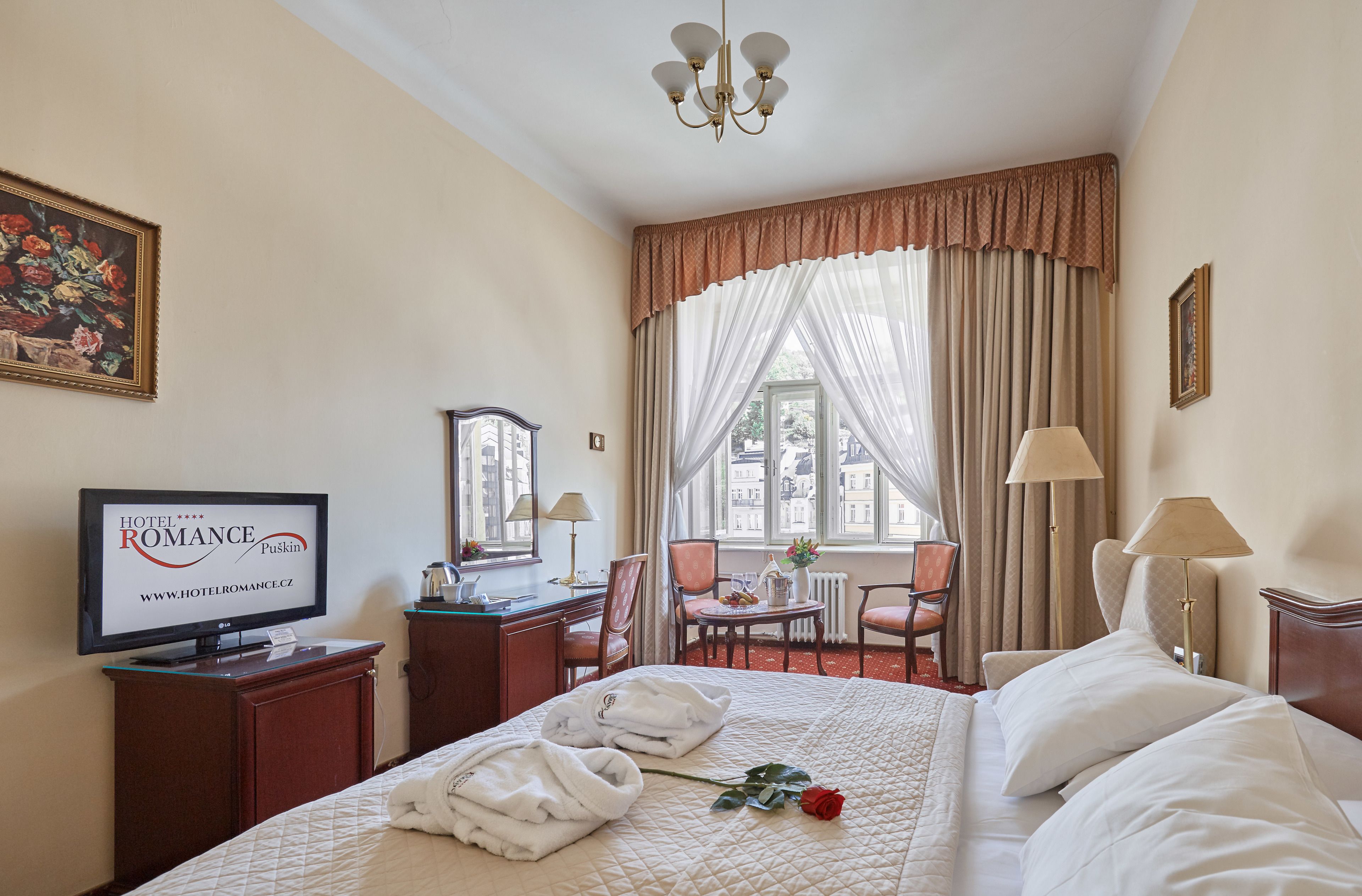 Una camera d'albergo con un letto, una scrivania, una sedia, una televisione e una finestra con tende.