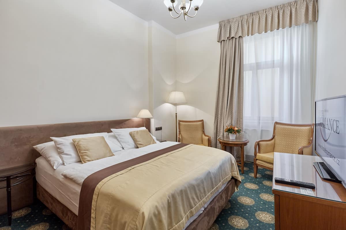 Ein Hotelzimmer mit einem Bett, zwei Stühlen, einem Schreibtisch und einem Fernseher sowie einer Lampe.