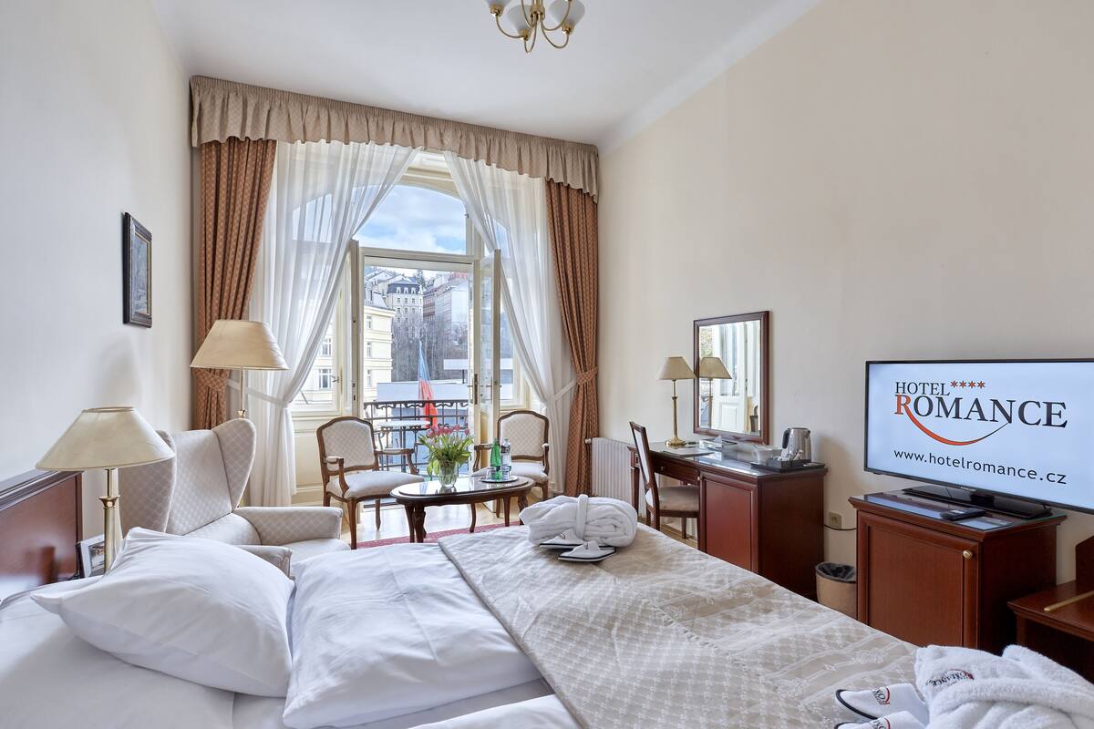 Ein Hotelzimmer mit Bett, Schreibtisch, Stuhl, Fernseher und einem fensterbepflanzten Fenster.