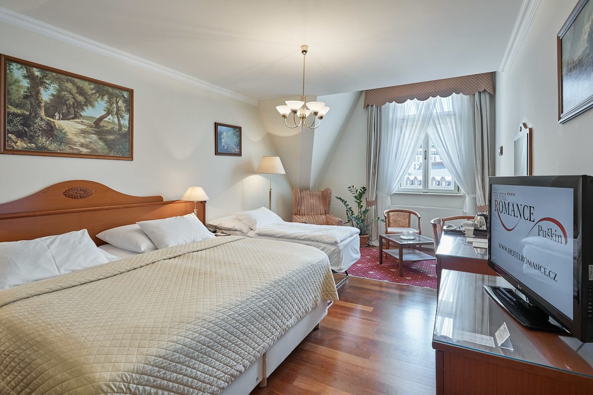Ein Hotelzimmer mit zwei Betten, einem Fernseher, einem Schreibtisch und einem Fenster mit Vorhängen.