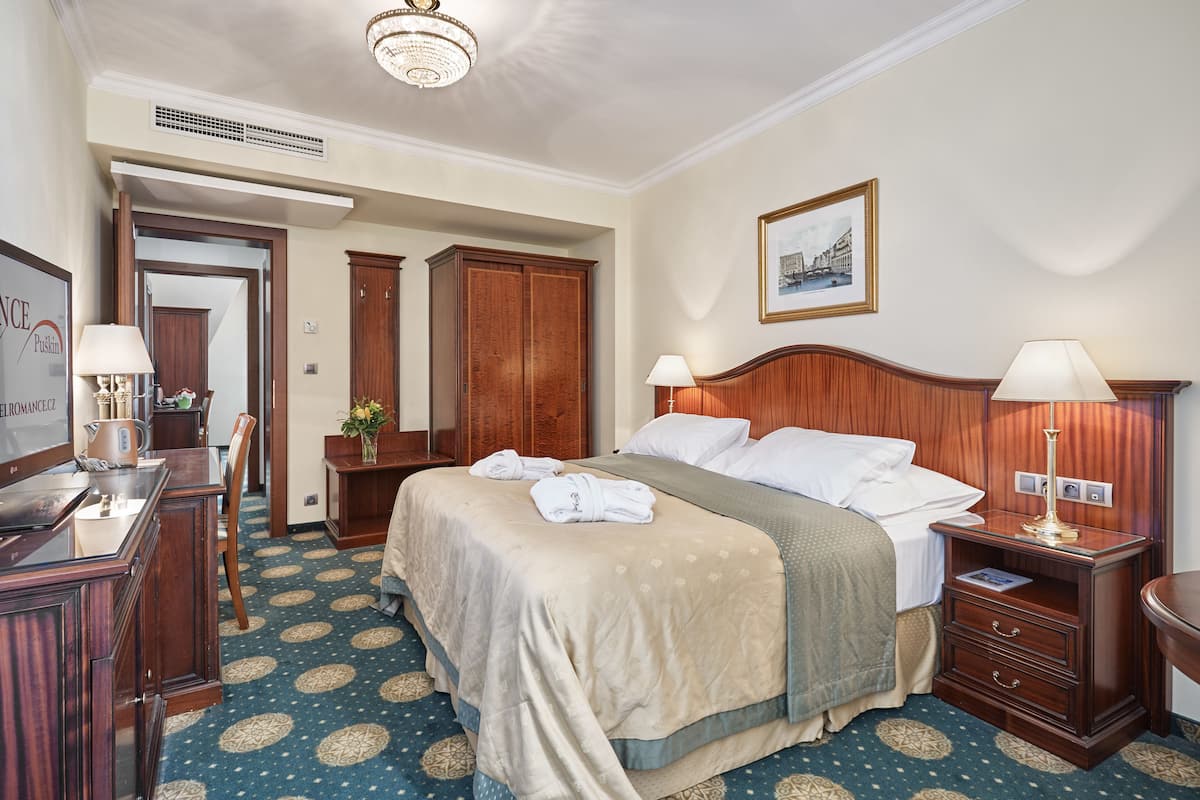 Ein Hotelzimmer mit einem großen Bett, zwei Nachttischen mit Lampen, einem Holzschrank, einem Schreibtisch mit Stuhl und einem gerahmten Bild an der Wand.